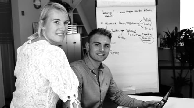 Schwarz-weiß-Bild. Simon und Ricarda schauen direkt in die Kamera und lächeln.