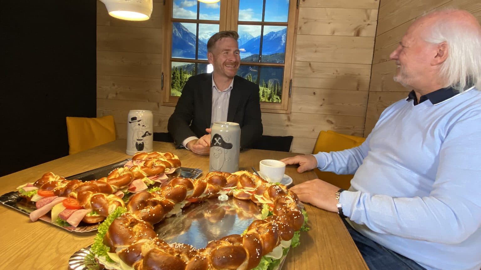 Interview zwischen Bernd Wandt, CEO von ServiceFactum und Mike Deiß, CEO von eggs unimedia. Beide schauen sich lachend an. Vor ihnen liegt eine Brezel in Form einer 10 als Sinnbild für die 10 erfolgreichen Jahre der gemeinsamen Partnerschaft.